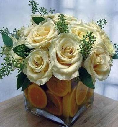 10 cream Rose arrangement with Orange slices in a square vase.