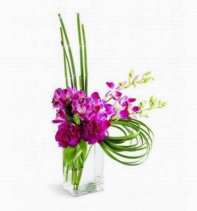 Fuchsia dendrobium orchids, purple alstroemeria and purple carnations in a contemporary glass vase.
