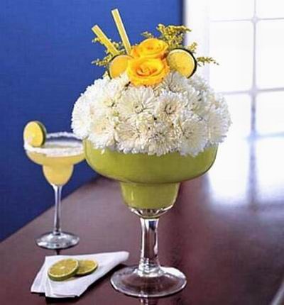 Yellow roses, white cushion pom, faux lime and more, arranged in an oversized margarita glass. (if martini glass is not available, a clear vase will be substituted)