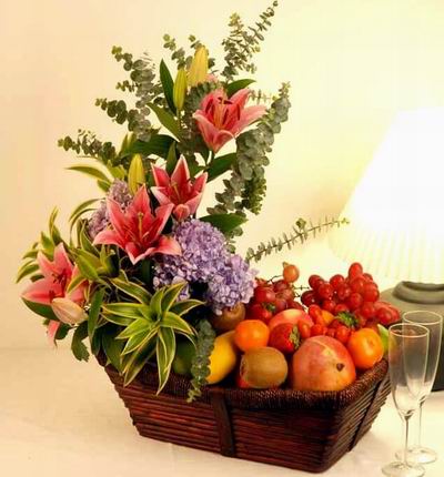 Flower basket of 4 pink open Lily Buds, purple Hydrangea, Leaves and plant fillers with Globe Grapes, 2 Peaches, 2 Tangerine Oranges, 2 Kiwis, 2 Mangos, and 5 Strawberries.