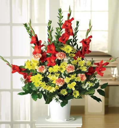 A vibrant sympathy arrangement overflowing with red gladiolus, bi-color carnations, yellow alstroemeria and more. Hand arranged by a florist, it is available for delivery to a funeral home to be displayed on a stand. Floral arrangement measures approximately 35