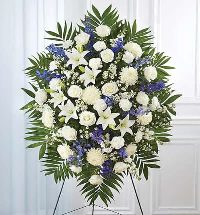 Show your support and heartfelt compassion by sending this comforting white and blue arrangement. The blue and white standing spray is created with flowers including blue delphinium, white roses, white lilies and more. Medium (shown) measures approximately 46